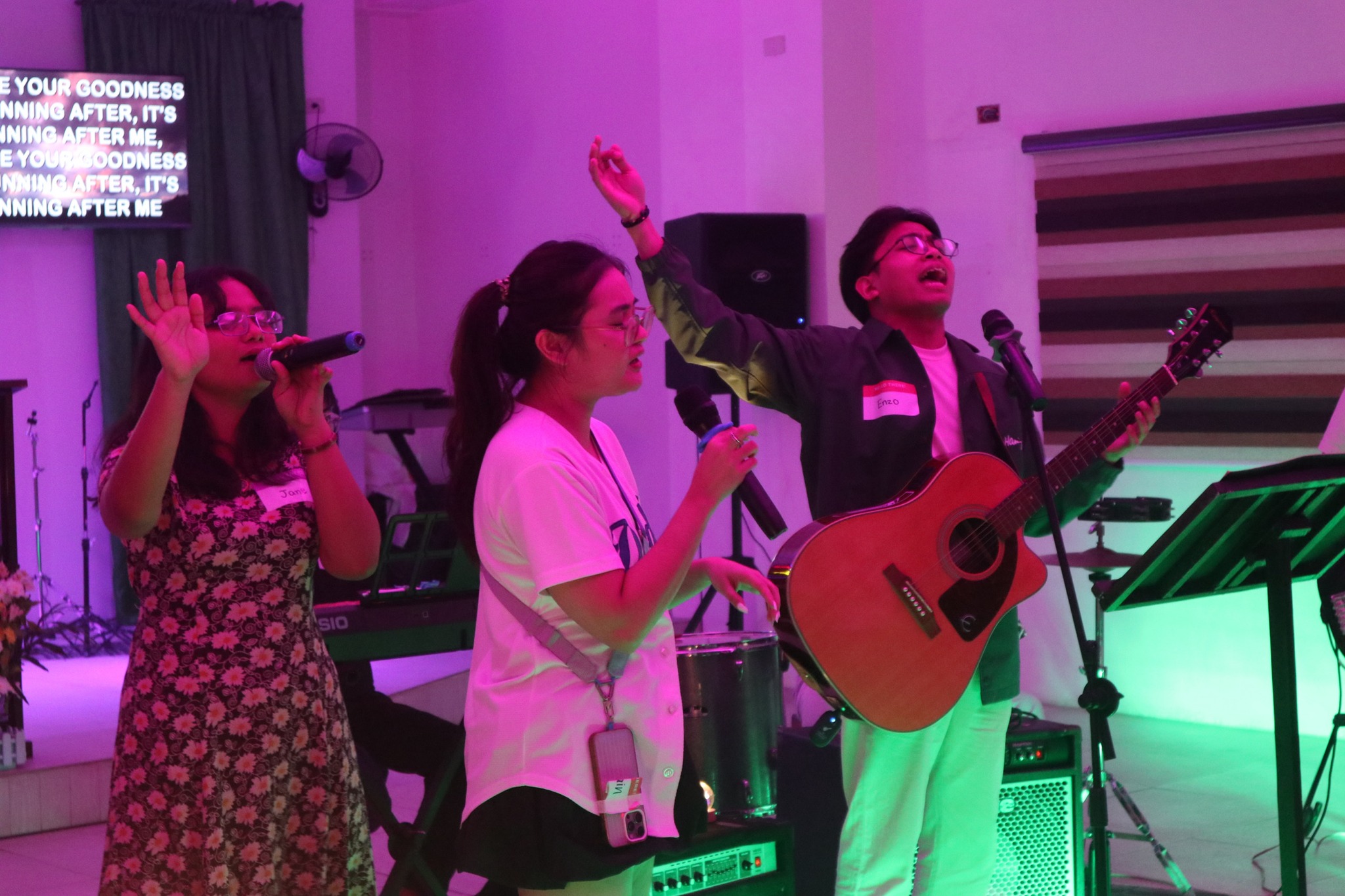 Three Ignite 2025 singers leading worship, with hands raised and an acoustic guitar