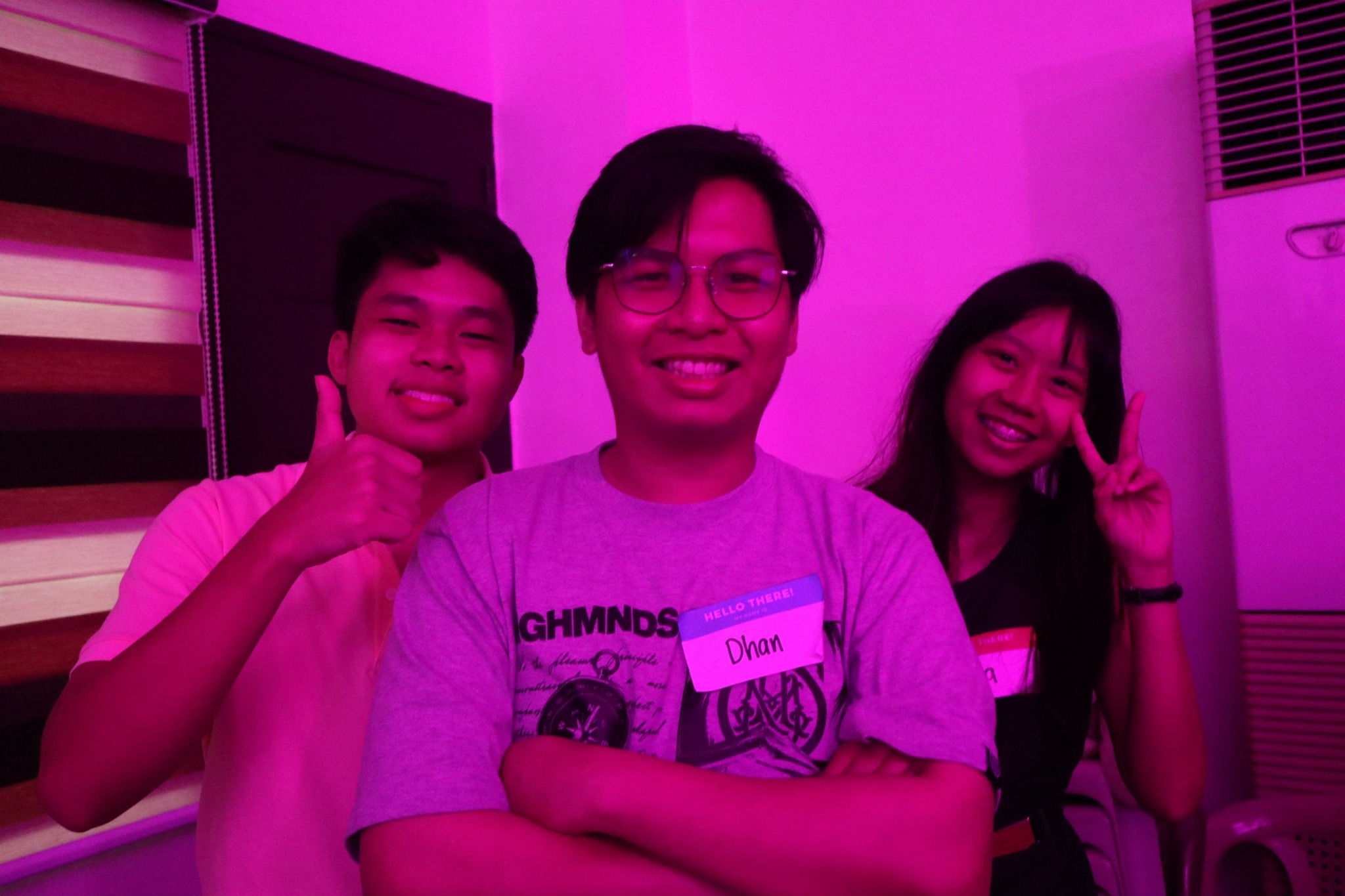 Three friends smiling for a photo in the pink lights of Ignite 2025